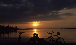 Zwei Radfahrer sitzen Rücken an Rücken und genießen einen wunderschönen Sonnenuntergang über dem Bodensee.