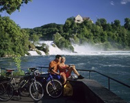 Ein Radlerpärchen hat es sich auf einer Mauer vor dem Rheinfall von Schaffhausen gemütlich gemacht.