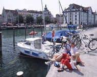 Eine Familie mit 2 Kindern sitzt am Ufer des Bodensees und beobachtet das Treiben um sie herum.