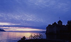 Ein Pärchen hat seine Fahrräder vor der Kulisse von Schloss Chillon am Ufer des Genfersees abgestellt und genießt das romantische Abendlicht.