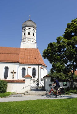 Die Klosterkirche Andechs an der ein Fahrradfahrer vorbei fährt