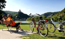 Zwei Radler sitzen gemütlich auf einer Bank und blicken über die Mosel.