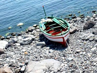 Ein rot-weiß-grünes Ruderboot liegt auf einem sizilianischen Kiesstrand.