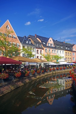 Mit roten Blumen geschmückter Kanal der Mosel mit Blick auf die Promenade von Saarburg