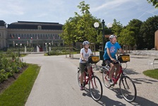 Zwei Radfahrer - ein Mann und eine Frau - auf einem asphaltierten Radweg beim Casino von Bad Ischl.