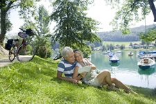 Ein Pärchen macht auf einer Wiese am Ufer des Mattsees Pause und studiert auf der Karte den weiteren Verlauf der heutigen Radetappe.