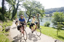 Vier Radler - drei Frauen und ein Mann - fahren auf einem asphaltierten Radweg am Ufer des Mattsees entlang.