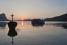 Sonnenuntergang über dem Kreuzstein im und einem Passagierschiff auf dem Mondsee.