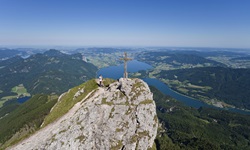 Eine Person steht auf dem Gipfel des Schafbergs und genießt die wunderbare Aussicht auf die Seenlandschaft des Salzkammergutes.