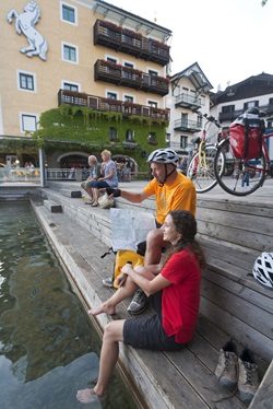 Zwei Radler machen vor der Kulisse des Weißen Rössls in St. Wolfgang am Seeufer Pause.