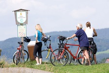 Eine Radlergruppe steht an einem Schild mit der Aufschrift Naturschutzgebiet und blickt in die Landschaft des Salzkammerguts