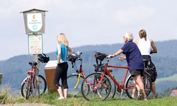 Eine Radlergruppe steht an einem Schild mit der Aufschrift Naturschutzgebiet und blickt in die Landschaft des Salzkammerguts