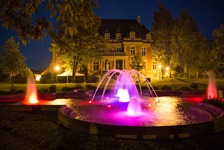 Blick auf den nächtlich rot-lila beleuchteten Brunnen und das beleuchtete Rathaus in Sarreguemines