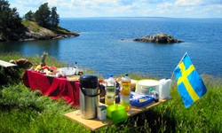 Ein appetitlich auf Holztischen angerichtetes und mit einer schwedischen Fahne dekoriertes Picknick wartet in einer idyllischen Bucht in Südschweden auf die hungrigen Radler.