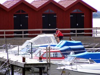 Bootshäuser in Schweden, auf dem Steg fährt ein Radler entlang und sieht sich die angelegten Boote an