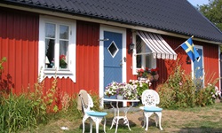 Ein typisches Schwedenhaus mit rotem Anstrich und blauen Türen, davor steht ein Cafétisch mit zwei Stühlen
