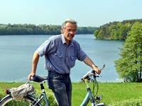 Ein Mann schiebt sein Fahrrad - hinter ihm eine Wiese und ein See
