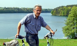 Ein Mann schiebt sein Fahrrad - hinter ihm eine Wiese und ein See