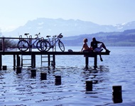 Ein Pärchen, das auf der Schweizer Seenroute unterwegs ist, hat seine Räder auf einem hölzernen Steg abgestellt und genießt den Blick über einen der Seen.