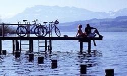 Ein Pärchen, das auf der Schweizer Seenroute unterwegs ist, hat seine Räder auf einem hölzernen Steg abgestellt und genießt den Blick über einen der Seen.