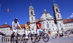 Drei junge Radlerinnen fahren auf der Schweizer Seenroute am markanten Kloster Einsiedeln vorbei.