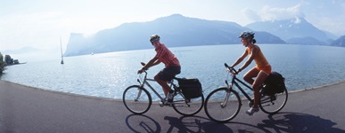 Ein Mann und eine Frau radeln auf der Schweizer Seenroute an einem See entlang.