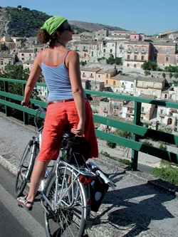 Eine Radlerin steht auf einer Brücke und betrachtet die Stadt Ibla Ragusa.