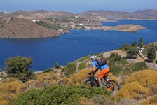Ein Mountainbiker fährt einen Trail auf der Radreise Inselhüpfen Griechische Ägäis Mitte hinab, während im Hintergrund das Meer zu sehen ist
