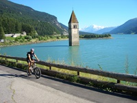 Ein Radler fährt auf dem Etsch-Radweg am Reschensee und dem versunkenen Kirchturm von Alt-Graun vorbei.