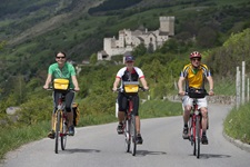 Drei Radler fahren nebeneinander auf dem Etsch-Radweg; im Hintergrund ist die mächtige Churburg zu erkennen.