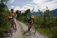 Ein Radlerpärchen lässt auf einem weiß gekiesten Abschnitt des Etsch-Radwegs die schneebedeckten Dolomitengipfel hinter sich.