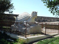 Blick auf eine Steinskulptur: Ein Schildkrötenkörper mit einem menschlichen Gesicht und langen Haaren