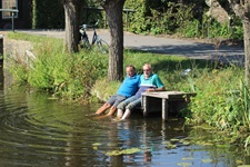 Zwei Radler machen an einem See Pause und lassen die Füße ins Wasser baumeln.