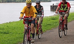 Drei Radler fahren auf einem Radweg entlang des Ufers