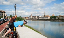 Zwei Radler machen am Ufer des Arno Pause und schauen auf die Skyline von Florenz.