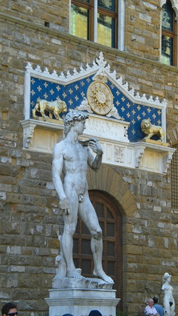 Blick auf eine männliche Statue vor einem Haus, das mit einem Ornament mit zwei Löwen und einer Sonne bestückt ist