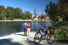 Ein Paar steht am Ufer der Donau und blickt zum Ulmer Münster, hinter sich sind ihre Räder abgestellt