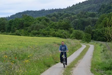 Ein gepflasteter Radweg durch Wiesen und Felder, auf dem ein Radler fährt