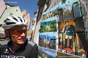 Radfahrer sieht sich Postkarten in einem Kartenständer in Füssen an