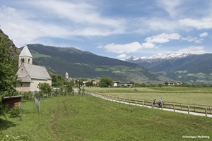 Zwei Radfahrer auf dem Radweg der Via Claudia Augusta fahren an einer Kapelle im Vinschgau vorbei