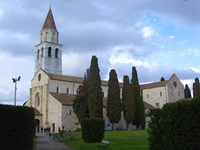 Zypressen und eine Gruppe (Rad-)Touristen vor der Basilika von Aquileia.