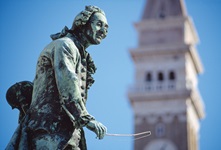 Die Bronzestatue des Geigers Giuseppe Tartini in Piran. Im Hintergrund ist unscharf der Turm der Kirche St. Georg zu sehen.