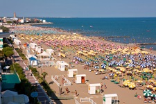 Strandkörbe, Sonnenschirme und Touristen am voll besetzten Strand von Caorle.