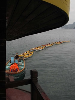 Eine vietnamesische Dschunke zieht Boote hinter sich her