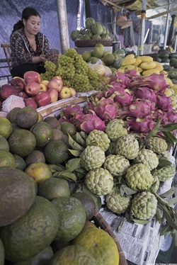 Eine vietnamesische Frau verkauft an einem Marktstand Obst und Gemüse.