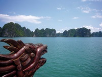 Blick vom Schiff auf die Ha Long Bucht in Vietnam. Der Bildvordergrund wird vom hölzernen Drachenkopf der Dschunke beherrscht.