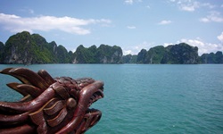 Blick vom Schiff auf die Ha Long Bucht in Vietnam. Der Bildvordergrund wird vom hölzernen Drachenkopf der Dschunke beherrscht.
