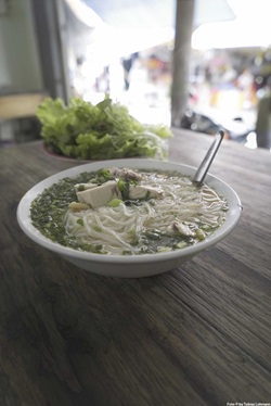 Ein Teller mit vietnamesischer Suppe, die unter anderem Glasnudeln und Fleisch enthält, steht auf einem hölzernen Tisch.