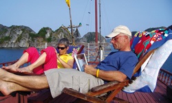 Ein Mann und eine Frau sitzen an Deck einer Dschunke in Liegestühlen und entspannen sich bei einer interessanten Lektüre.