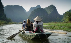 Teilnehmer einer Inselhüpfen-Reise fahren mit dem Ruderboot in ein verstecktes Tal bei Tam Coc in Vietnam.